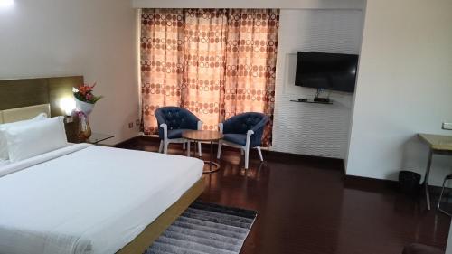 a hotel room with a bed and two chairs and a television at Rosewood International Hotel in Bengaluru