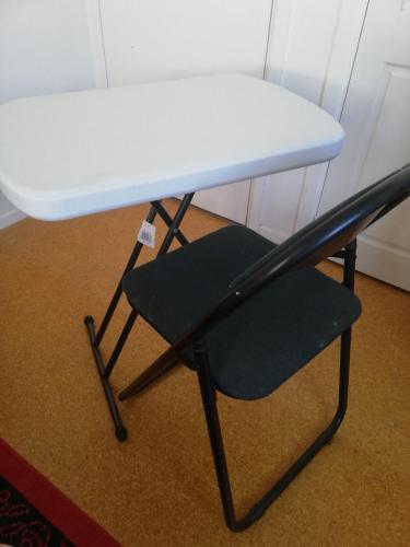 a chair under a table with a white desk at Songbird Sleepout with bathroom and mini kitchenette in Hamilton