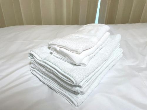 a pile of white towels stacked on a bed at Docaホテル セルフチェックイン in Fukuoka