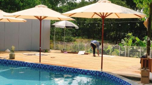a person standing next to a pool with two umbrellas at Dreamers Farm in Vinh Thanh