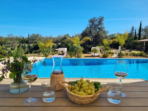 a table with wine glasses and a basket of fruit next to a pool at Cosy Guest House - Villa das Alfarrobas in Algoz