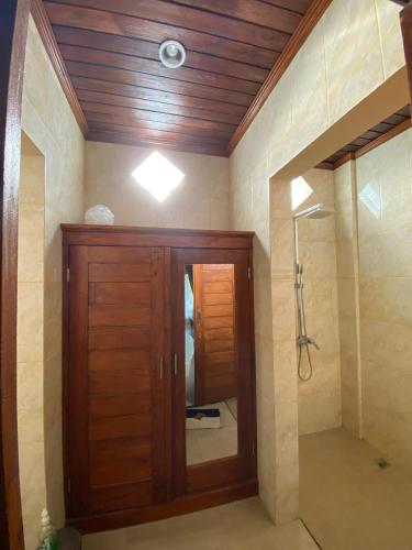 a bathroom with a shower with a wooden door and a mirror at Villa Indah Anugrah in Kubu