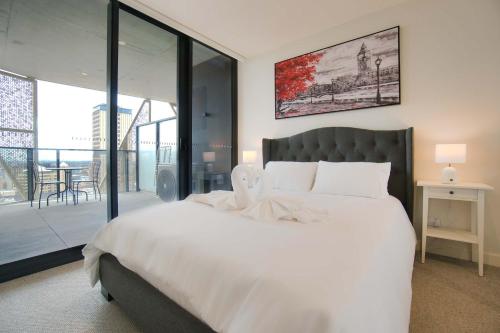une chambre avec un grand lit blanc et un balcon dans l'établissement Luxury Apartment in Rundle Mall with Beautiful City Views, à Adélaïde