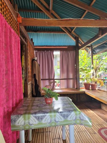 a table on a porch with pink curtains and a window at Mananambal Beach Huts - Family hut in Nagbalaye