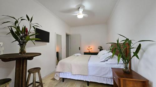 um quarto com uma cama com lençóis brancos e plantas em Quarto Pitangueiras em Florianópolis