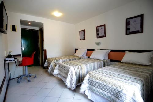 a hotel room with two beds and a red chair at Rede Andrade Mar Hotel - Rio Vermelho in Salvador
