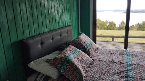 a bedroom with a bed with a green wall and a window at Cabañas Chillwe in Coñao