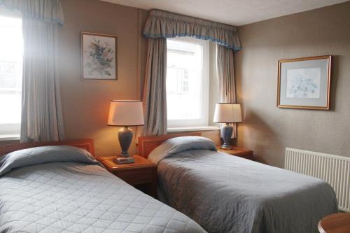two beds in a room with two lamps and a window at The Kings Head Hotel in Abergavenny