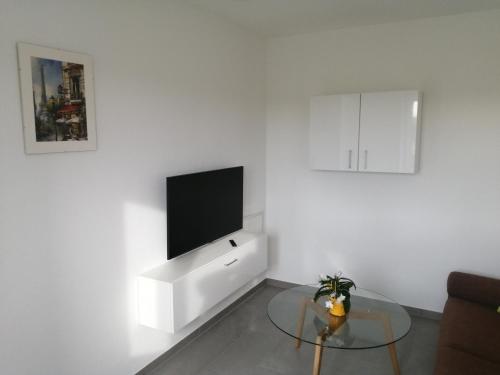 a white living room with a tv and a glass table at Allgäu-Ferienwohnung am Bachgrund in Argenbühl