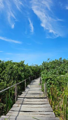 a wooden boardwalk through a field with a blue sky at Chalés Vila Irerê Itaúnas in Itaúnas