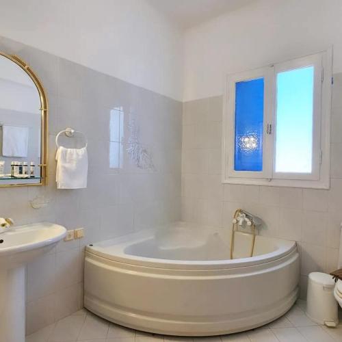 a white bathroom with a tub and a sink at SUNSET VILLA MILOS pera triovasalos in Triovasálos