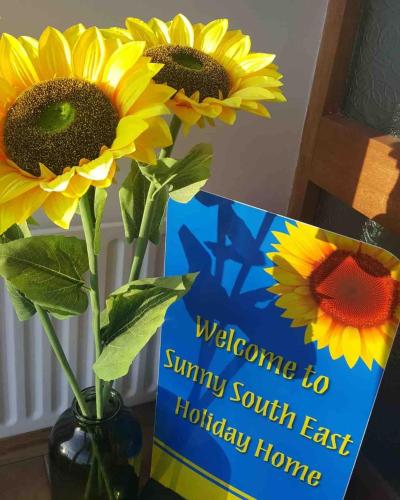 a sign with sunflowers in a vase with a welcome to sunny south at Sunny South East Holiday Home in Clashmore