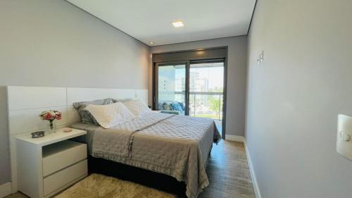 a bedroom with a bed and a table and a window at Pé na areia mod 5 Riviera de São Lourenço in Bertioga