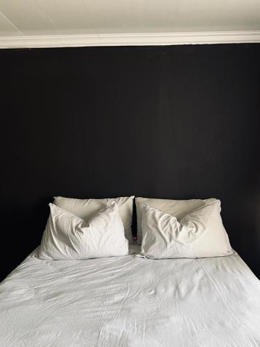 a bed with white pillows against a black wall at The Ripanga Nest in Nelspruit