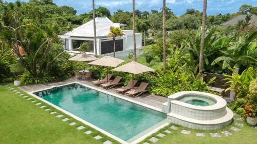 an outdoor pool with chairs and umbrellas next to a house at Villa Yenian by Villa Finder in Canggu