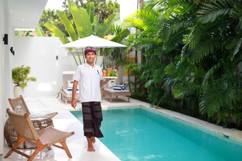 a man standing next to a swimming pool with an umbrella at Villa Sugi Umalas in Canggu
