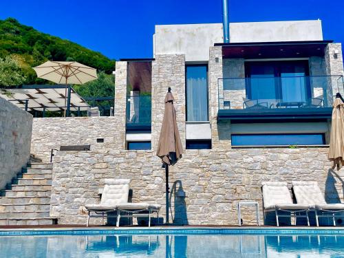 a swimming pool with two umbrellas and chairs next to a building at Allure Luxury Villas 2, Skiathos in Skiathos Town
