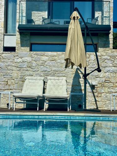 two chairs and an umbrella next to a swimming pool at Allure Luxury Villas 2, Skiathos in Skiathos Town