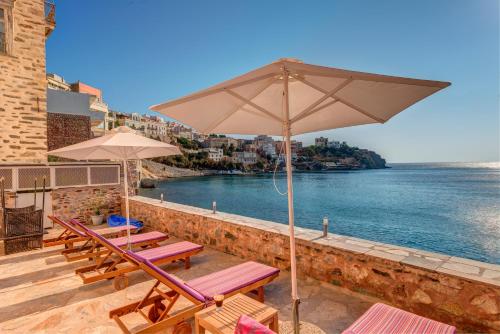 a group of chairs and umbrellas on a patio with the water at Apollonion Palace in Ermoupoli