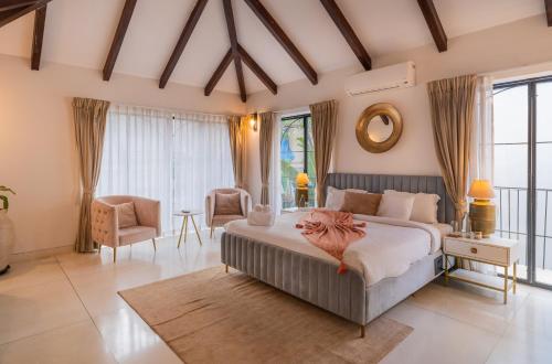 a bedroom with a bed and a chair and windows at ELIVAAS Bogenvilla Luxe 3 BHK Villa Near Ozran Beach in Assagao