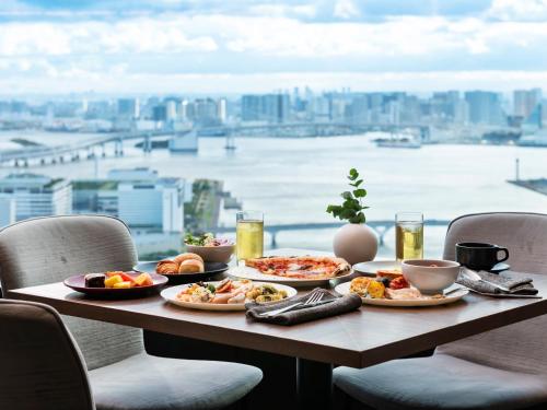 a table with plates of food and a view of a city at Mitsui Garden Hotel Toyosu Premier - Tokyo in Tokyo