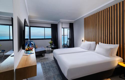 a bedroom with a large white bed and windows at Hotel Lake House Kinneret in Tiberias