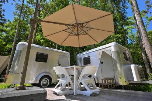 a table and chairs and an umbrella next to a trailer at glampark FREE AND EASY CAMP RESORT　三重県 in Komono