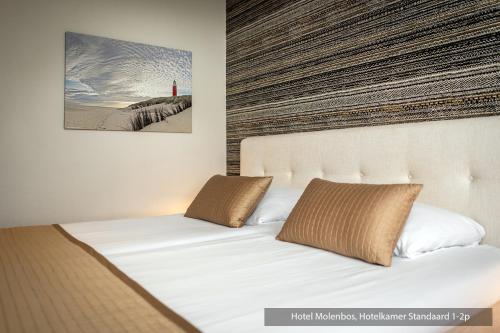 a bed with two pillows and a picture of a lighthouse at Hotel Molenbos Texel in De Cocksdorp