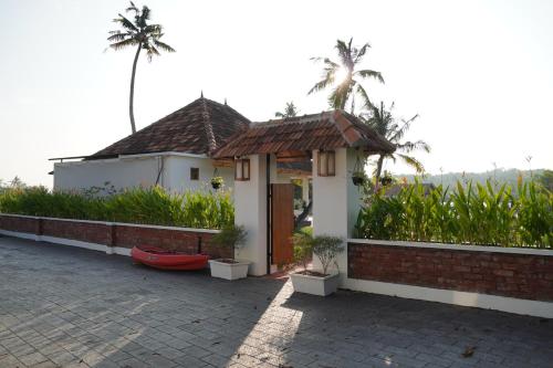 a small house with a porch and palm trees at Kaayal Villa Lakefront Retreat in Varkala in Varkala