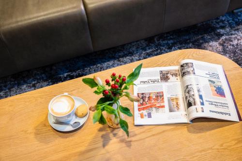 a newspaper and a cup of coffee and a vase with flowers at Novotel Amsterdam City in Amsterdam