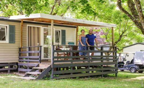un homme et une femme debout sur la terrasse couverte d'une maison dans l'établissement mobilhome terrasse ombragée 27m2, à Cahuzac-sur-Vère