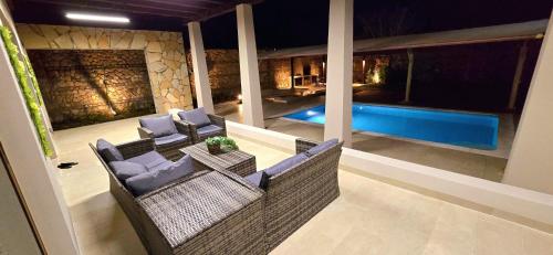 a patio with wicker chairs and a swimming pool at night at Wateera Jebel Sifah in As Sīfah