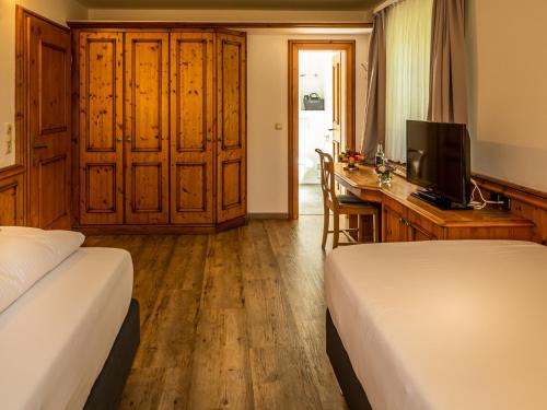 a bedroom with two beds and a desk with a television at Mäsers Allgäuherz in Wiggensbach
