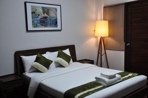 a bedroom with a bed with white sheets and green pillows at The Bedrooms Maeklong and Services Apartment in Samut Songkhram