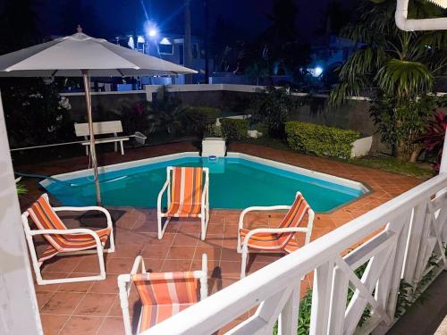a swimming pool with chairs and a table and an umbrella at Villa Le Guètali in Pointe d'Esny