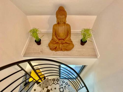 une statue assise sur une étagère avec deux plantes dans l'établissement Croissant de Lune - Cœur de Ville - Old Town, à Bayeux