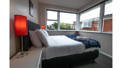 a bedroom with a bed with a red lamp and windows at 3-bedroom 2-bathroom Bright & Sunny Family home in Auckland