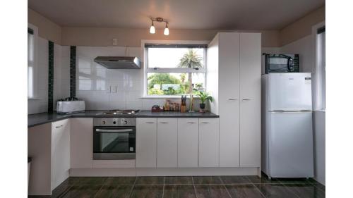 a kitchen with white cabinets and a white refrigerator at 3-bedroom 2-bathroom Bright & Sunny Family home in Auckland