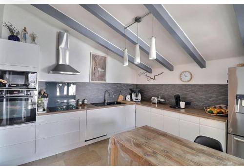 une cuisine avec des armoires blanches et une table en bois dans l'établissement Maison méditerranéenne 130m piscine Vaucluse, à Carpentras