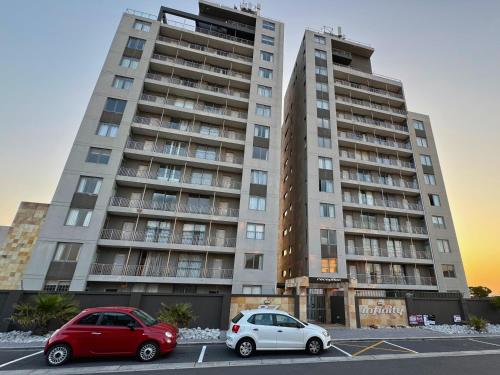 two cars parked in a parking lot in front of a building at Infinity - Stunning 1 bedroom apartment with sea & mountain views in Bloubergstrand