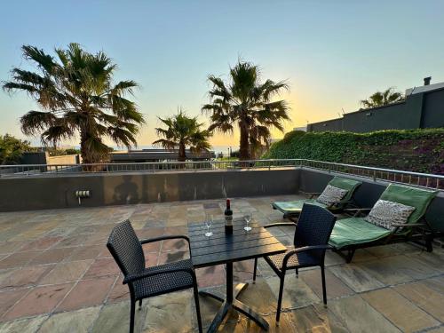 a table with chairs and a bottle of wine on a patio at Infinity - Stunning 1 bedroom apartment with sea & mountain views in Bloubergstrand