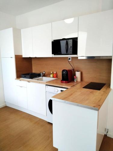 une cuisine blanche avec un évier et un micro-ondes dans l'établissement Vierzon Centre - joli T2- balnéo- wifi, à Vierzon