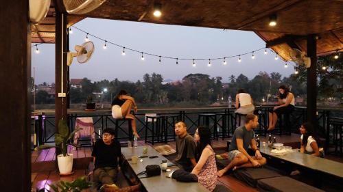 a group of people sitting on the deck of a restaurant at Funny Riverside Backpackers in Luang Prabang