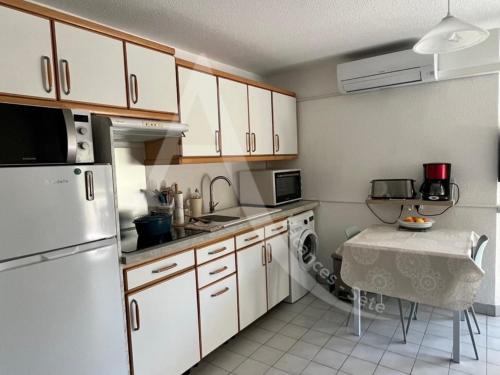 une cuisine avec des armoires blanches et une table à l'intérieur dans l'établissement Quartier plage 1 chambre Parking Climatisation Internet, à Sète