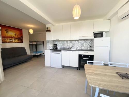 une cuisine avec des armoires blanches, une table et un canapé dans l'établissement AS21673 - Studio en rez de chaussée face au Canal, au Grau-du-Roi