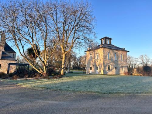 un ancien bâtiment avec une tour au-dessus d'un champ dans l'établissement Gîte du Haras de Vaugoubert, à Saint-Germain-de-Varreville