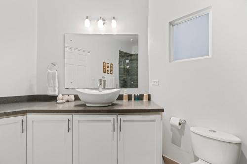 a white bathroom with a sink and a toilet at Newly Renovated Beachfront Condo with Inviting Minimalist Design, Pool & Balcony with Ocean Views in Playa Flamingo