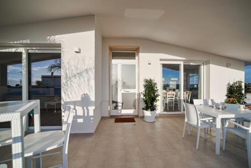 a dining room with white tables and chairs and windows at Villa N in Torre Suda