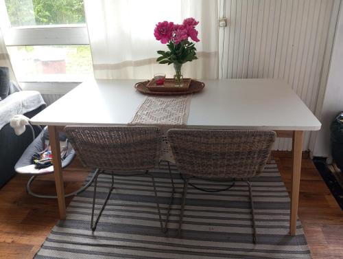 a white table with two chairs and a vase with pink flowers at Cozy cottage 30 min from Tallinn in Laitse