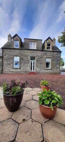 a stone house with two pots of plants in front of it at Marshill Farmhouse in Blackwood